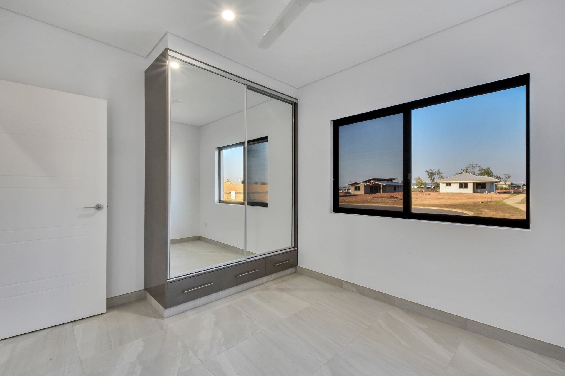 An empty bedroom with a large mirrored wardrobe and two windows.