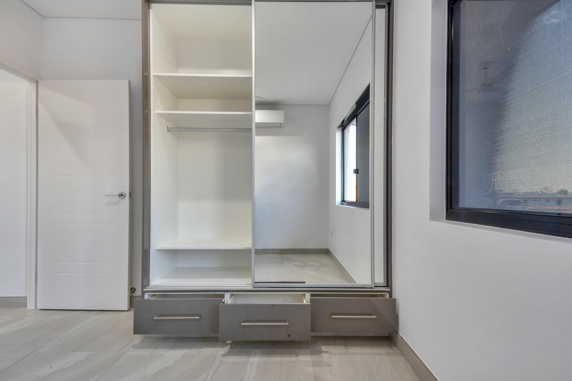 An empty bedroom with a sliding door wardrobe and a window.