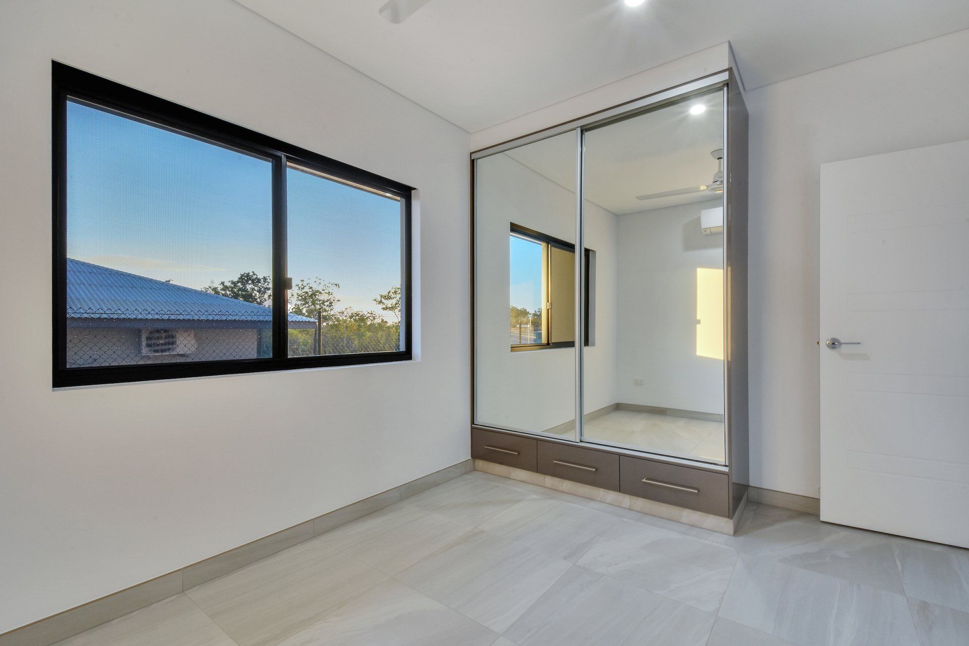 A bedroom with a large mirrored wardrobe and two windows.