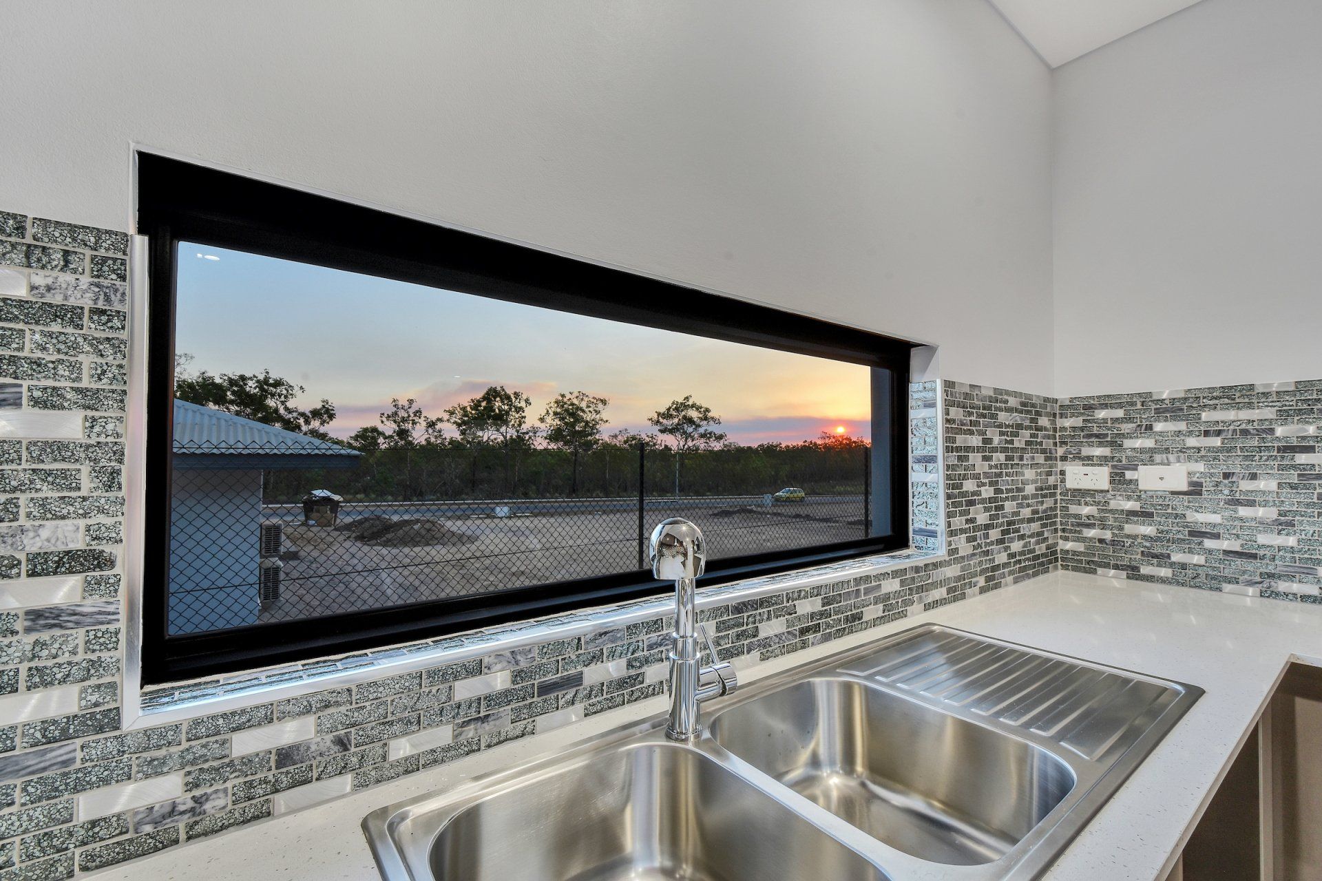 A kitchen with a sink and a large window with a view of the sunset.
