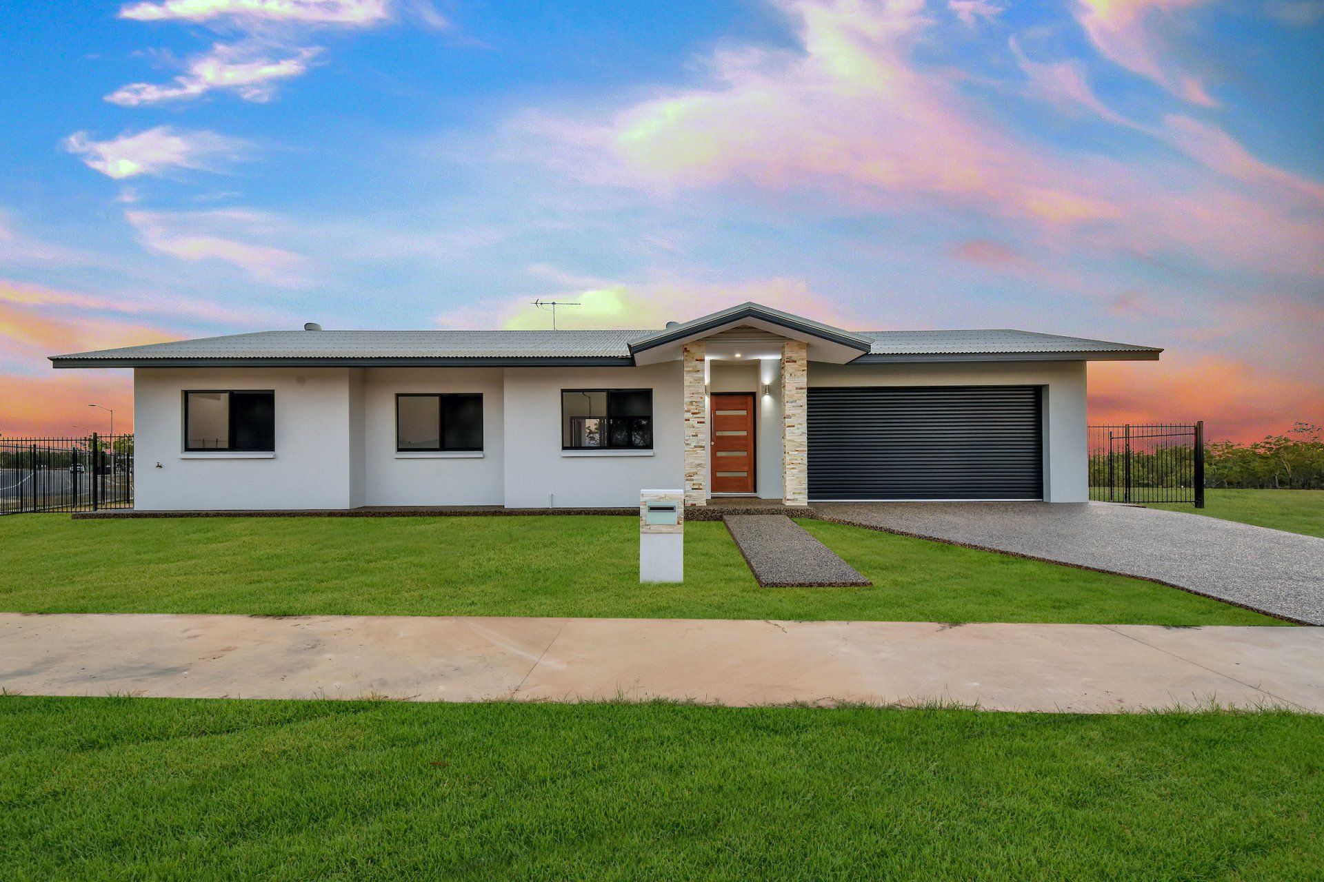A white house with a black garage door is sitting on top of a lush green field.