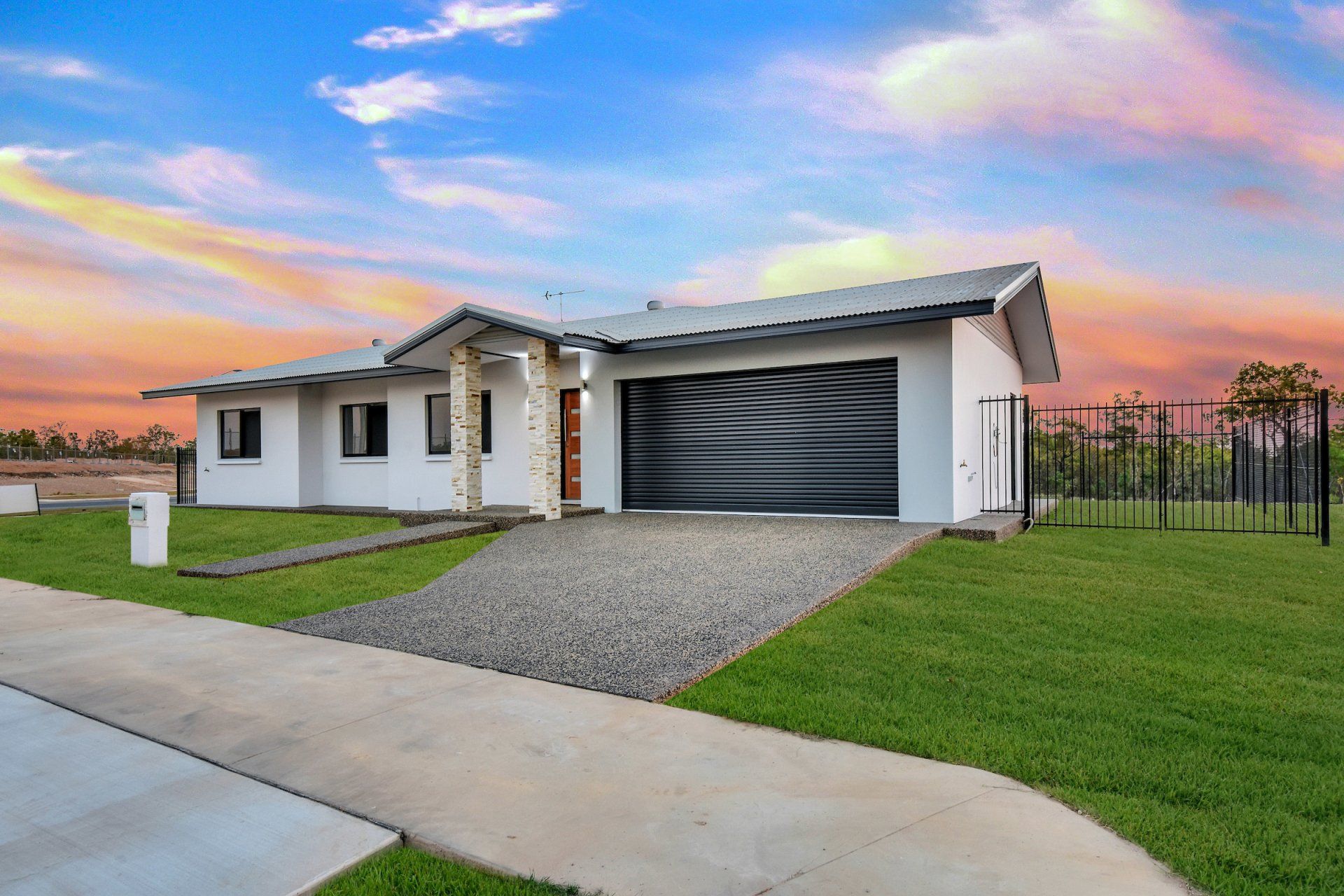 A white house with a black garage door is sitting on top of a lush green field.