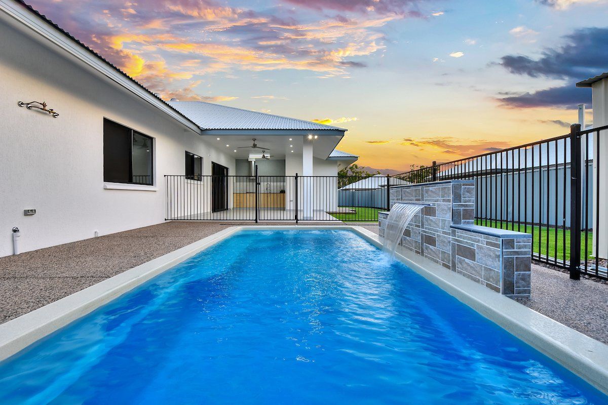 A large swimming pool is in the backyard of a house.