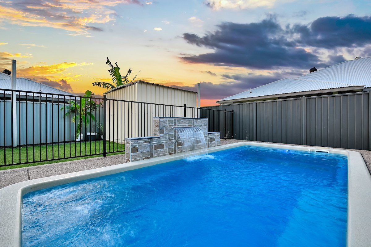 A large swimming pool with a waterfall in the backyard of a house.