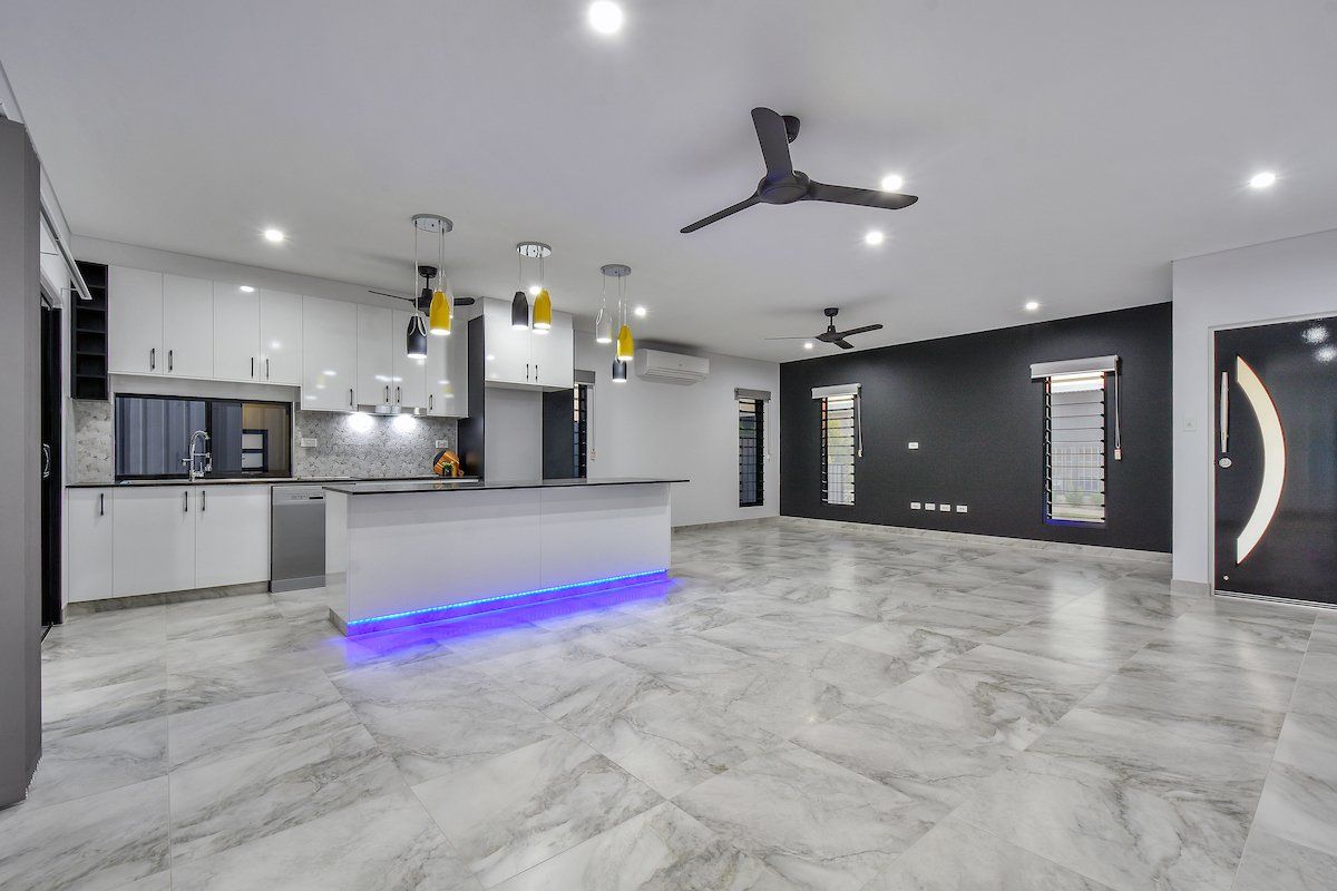 A large empty room with a kitchen and a ceiling fan.