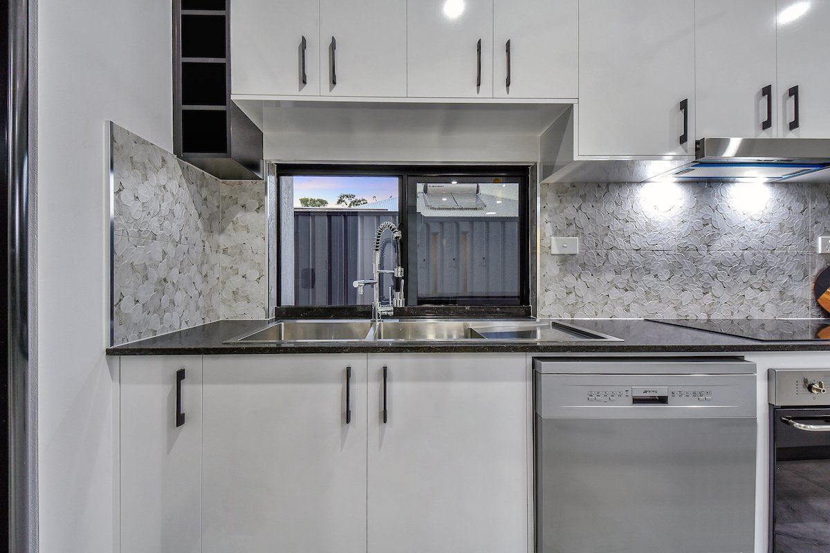 A kitchen with white cabinets , a sink , a stove , and a dishwasher.