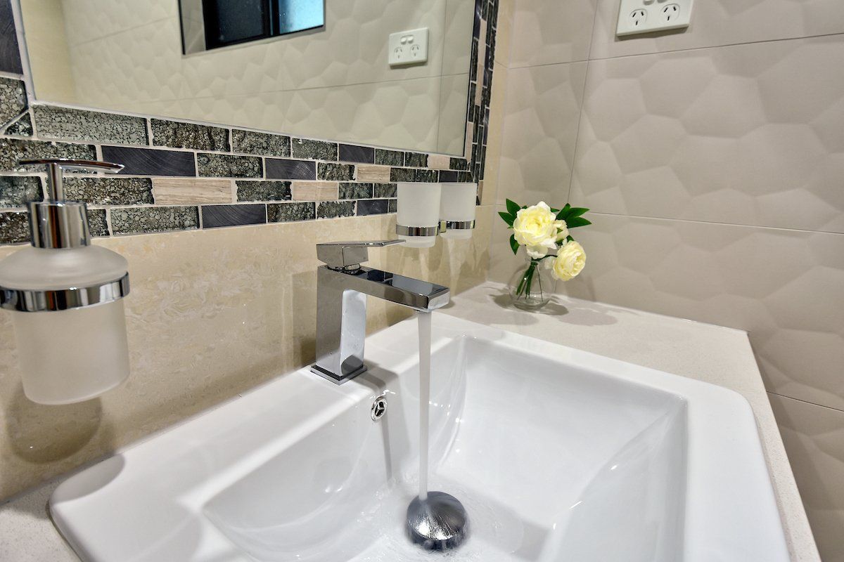 A bathroom sink with water running out of it and a vase of flowers on the counter.