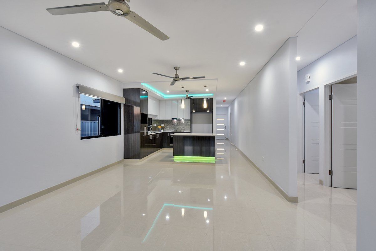 An empty room with a ceiling fan and a kitchen in the background.