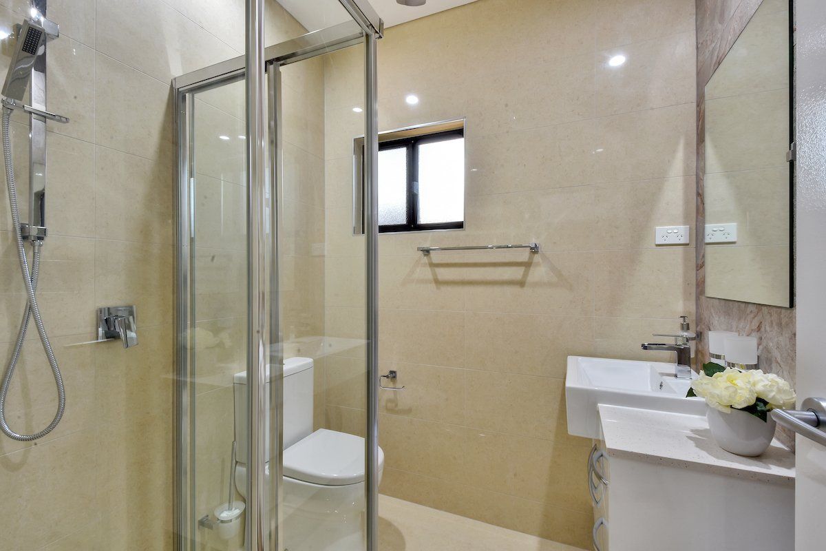 A bathroom with a toilet , sink , shower and mirror.