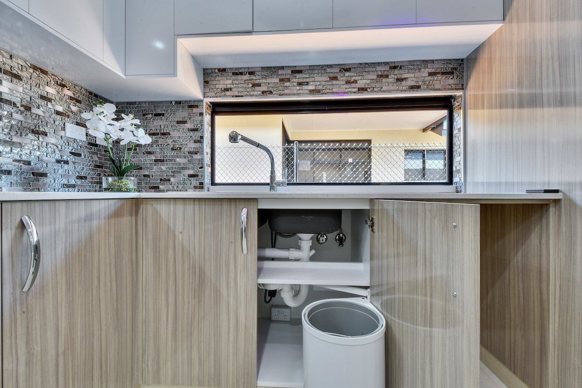 A kitchen with a sink and a trash can underneath it.