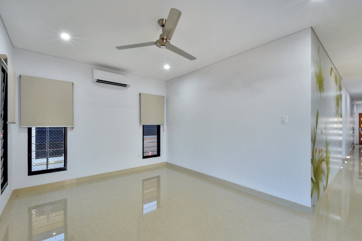 An empty room with a ceiling fan and two windows.