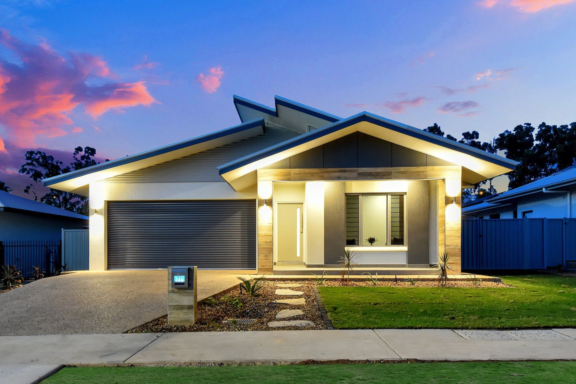 A modern house with a blue roof is lit up at night.