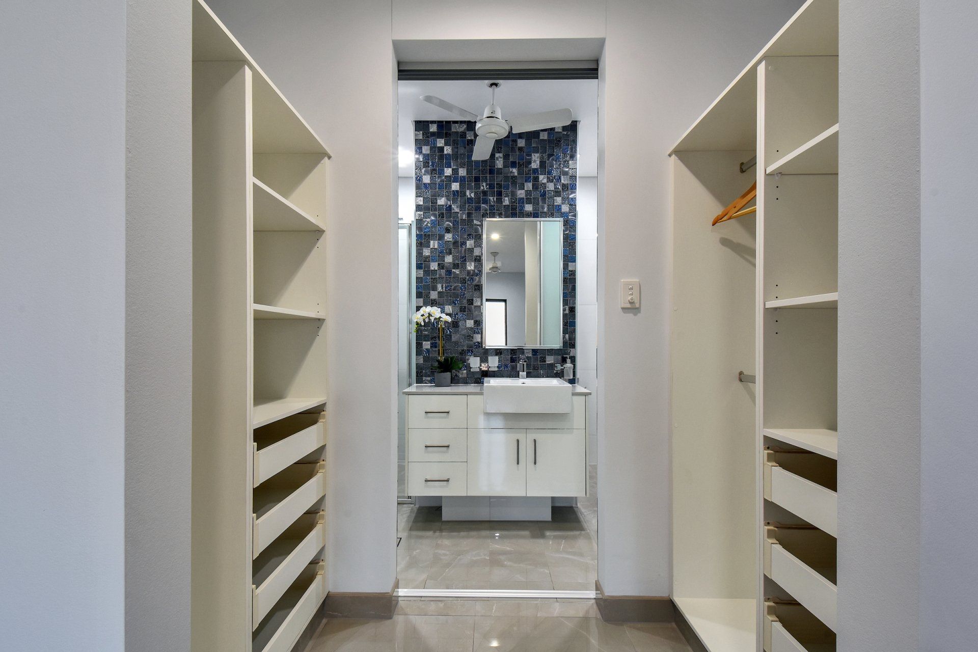 A walk in closet with a bathroom in the background.