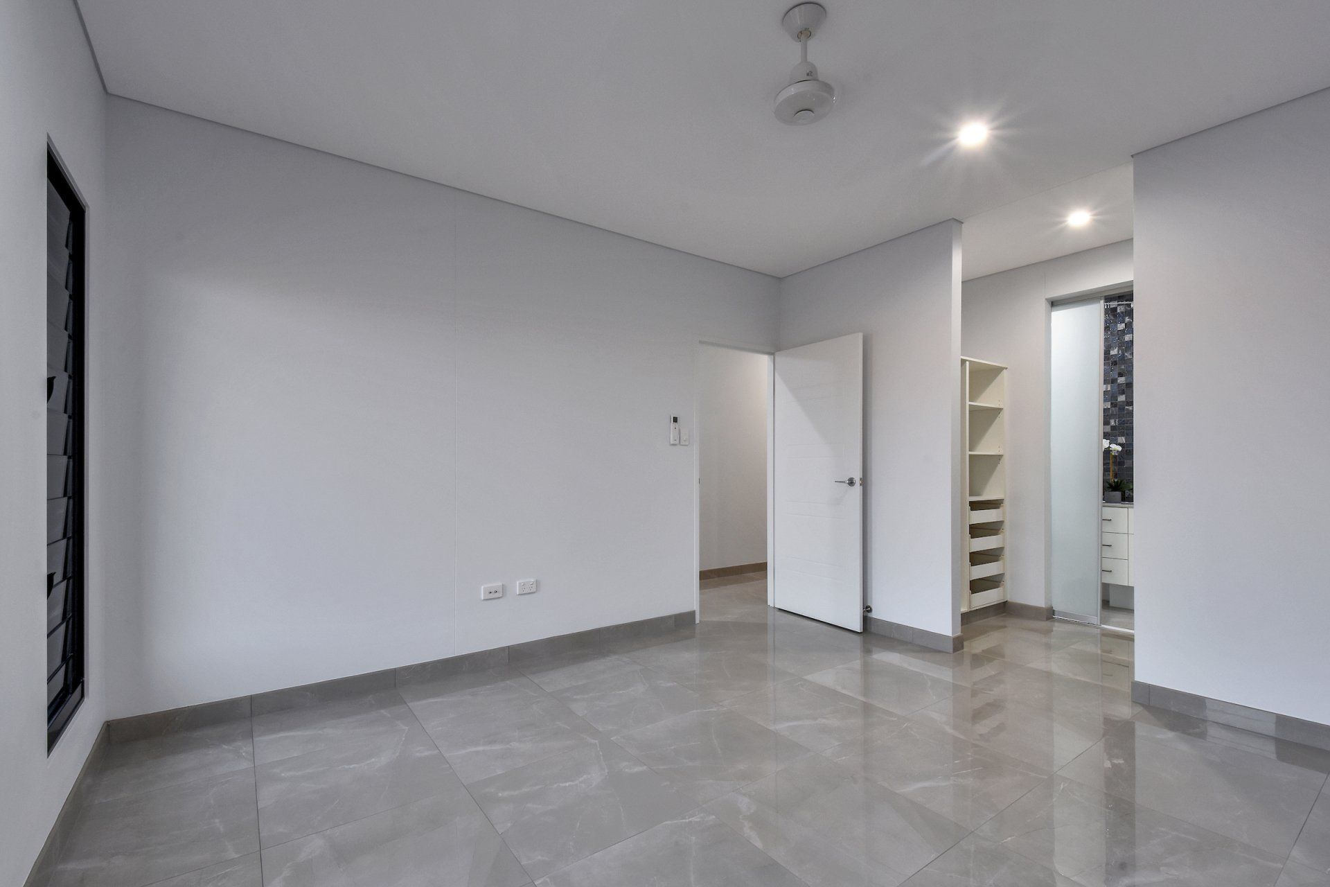 An empty room with white walls and a ceiling fan.