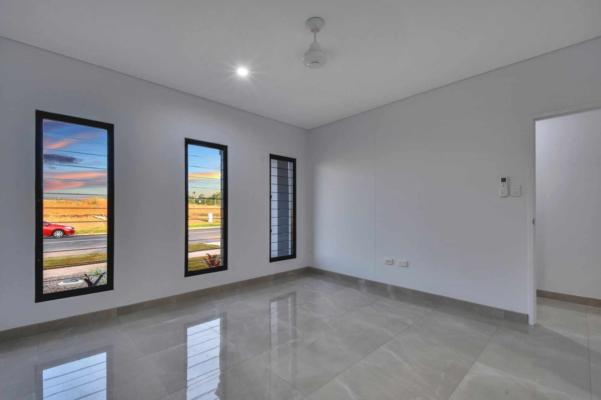 An empty room with three windows and a ceiling fan.