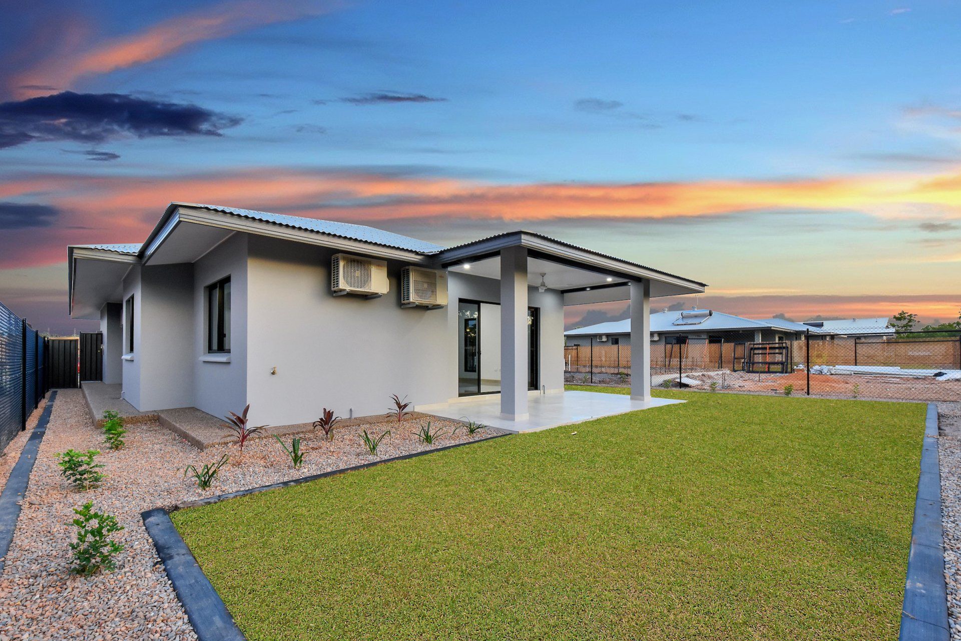 A house with a large lawn in front of it and a sunset in the background.