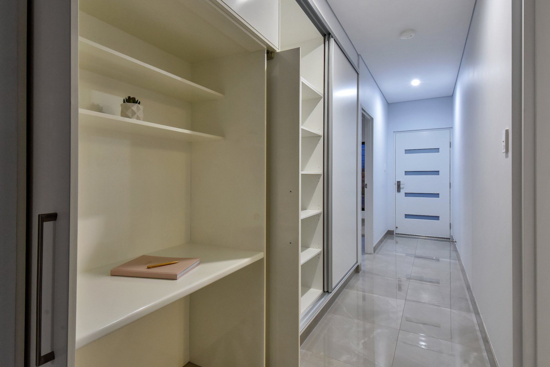 A long hallway with white shelves and a door.