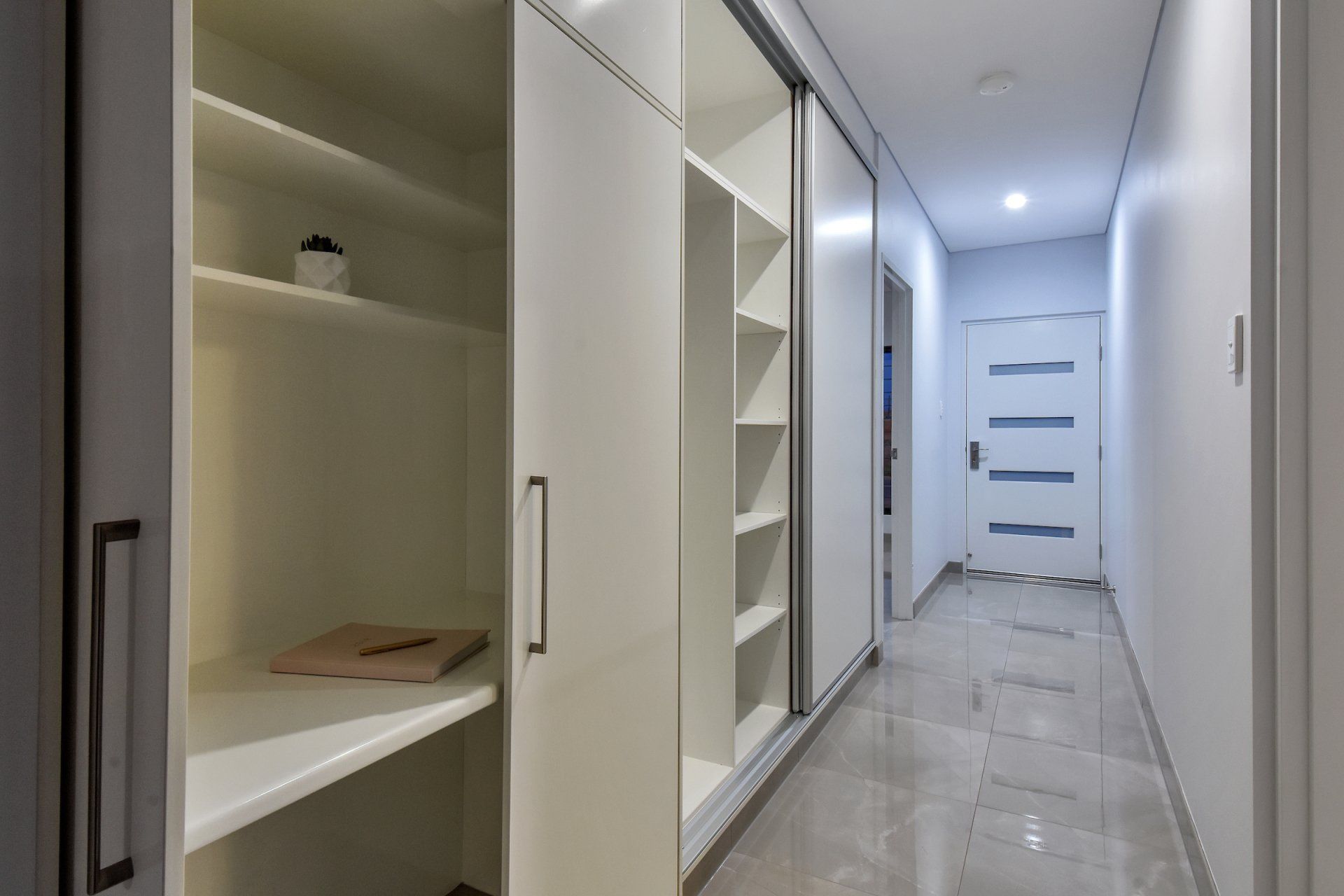 A long hallway with sliding doors and shelves in a house.