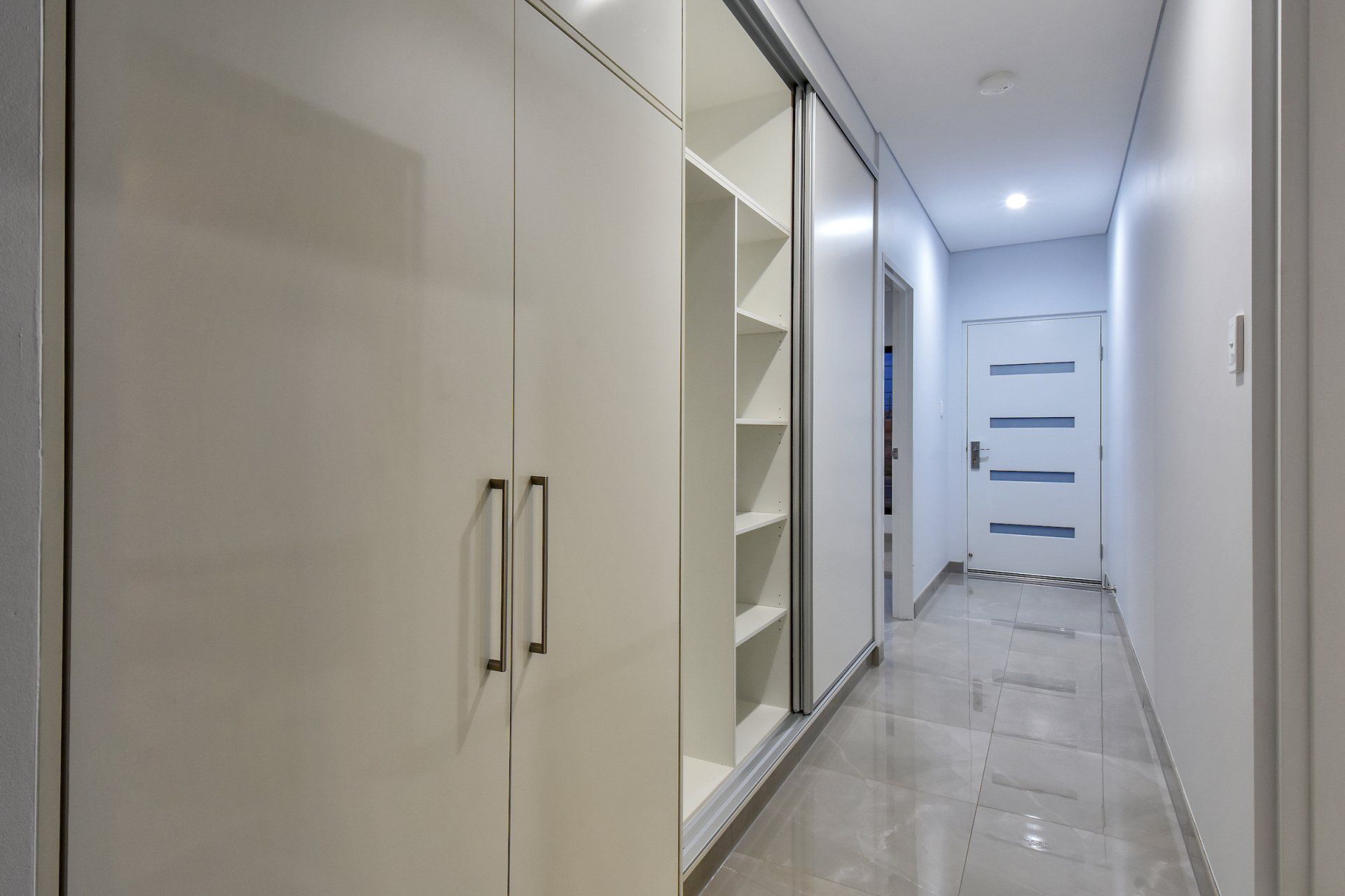 A long hallway with white cabinets and shelves and a door.