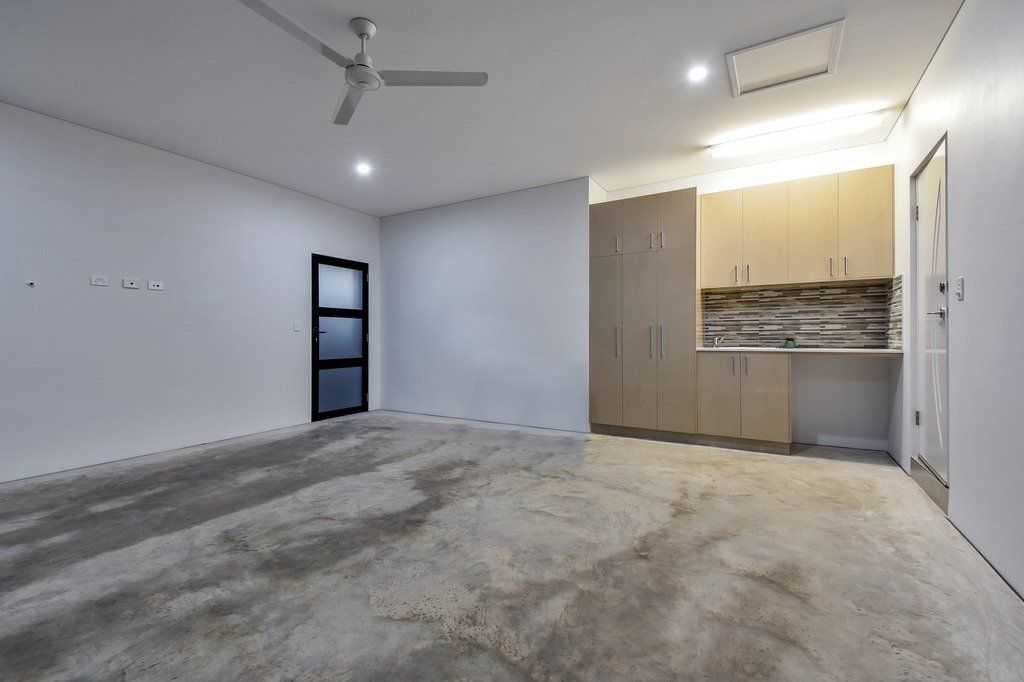 An empty room with a ceiling fan and a kitchen in the background.