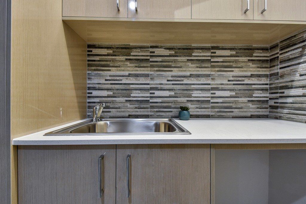 A kitchen with a sink , cabinets and a tiled wall.