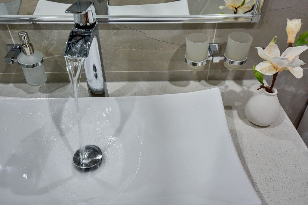 A bathroom sink with water running out of it and a vase of flowers on the counter.