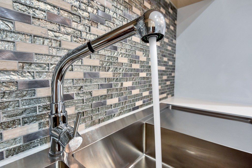 A close up of a kitchen sink with water running from the faucet.