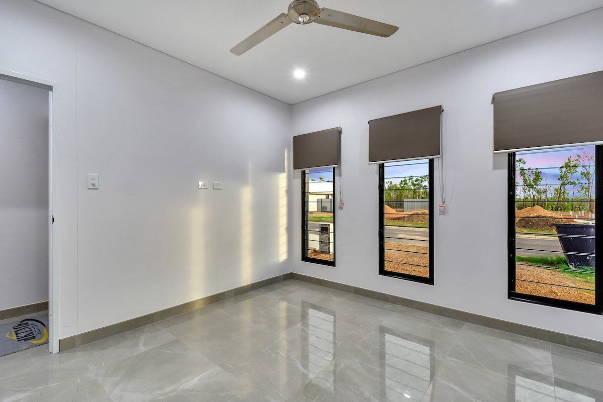An empty room with a ceiling fan and three windows.