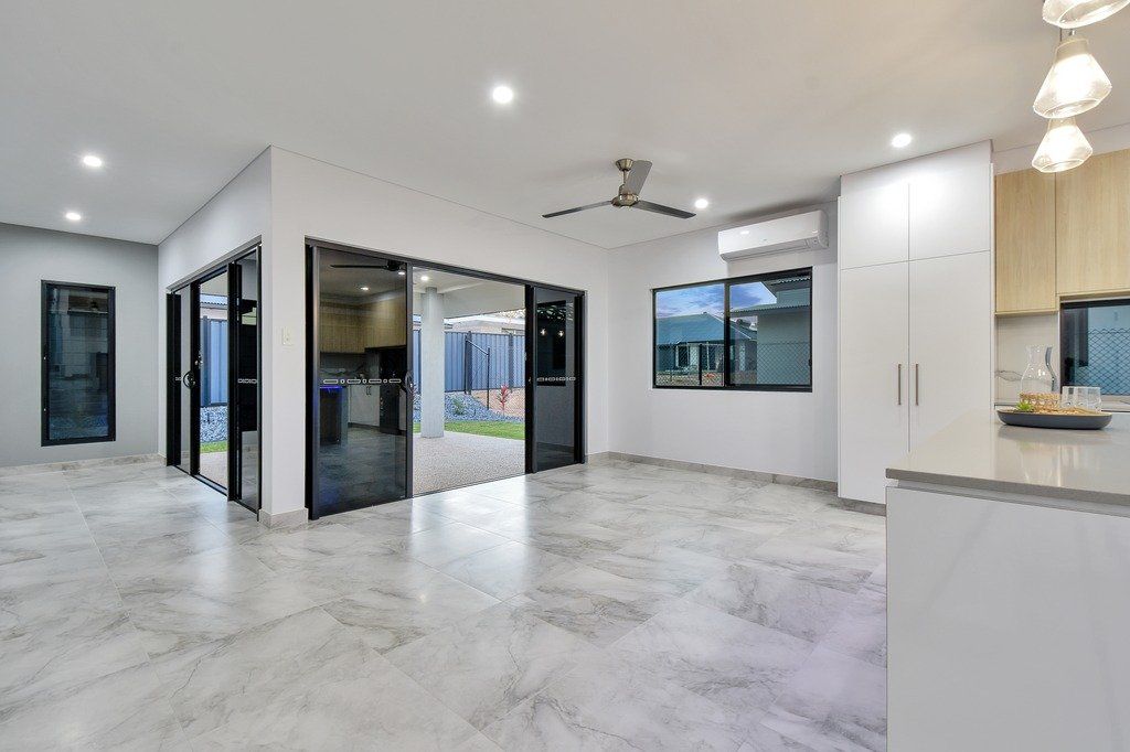 A large empty room with a ceiling fan and sliding glass doors leading to a kitchen.