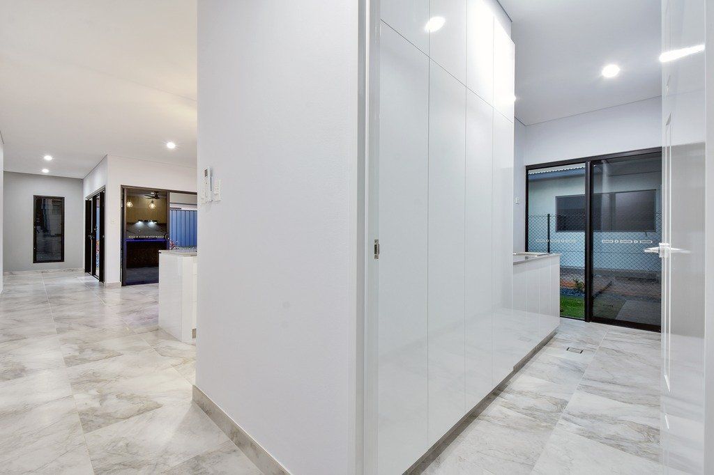 A hallway in a house with white cabinets and a marble floor.