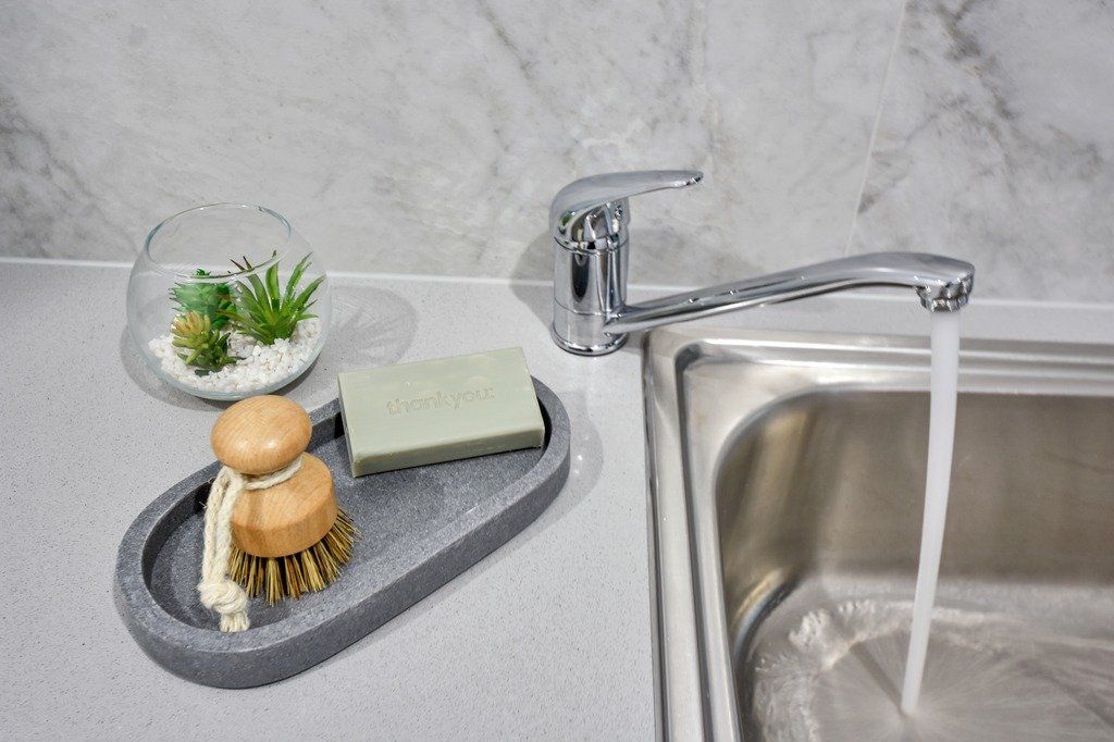 A kitchen sink with a soap dish and a brush on it.