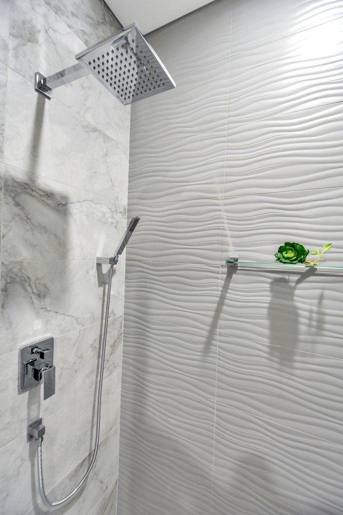 A bathroom with a shower head and a shelf with a flower on it.
