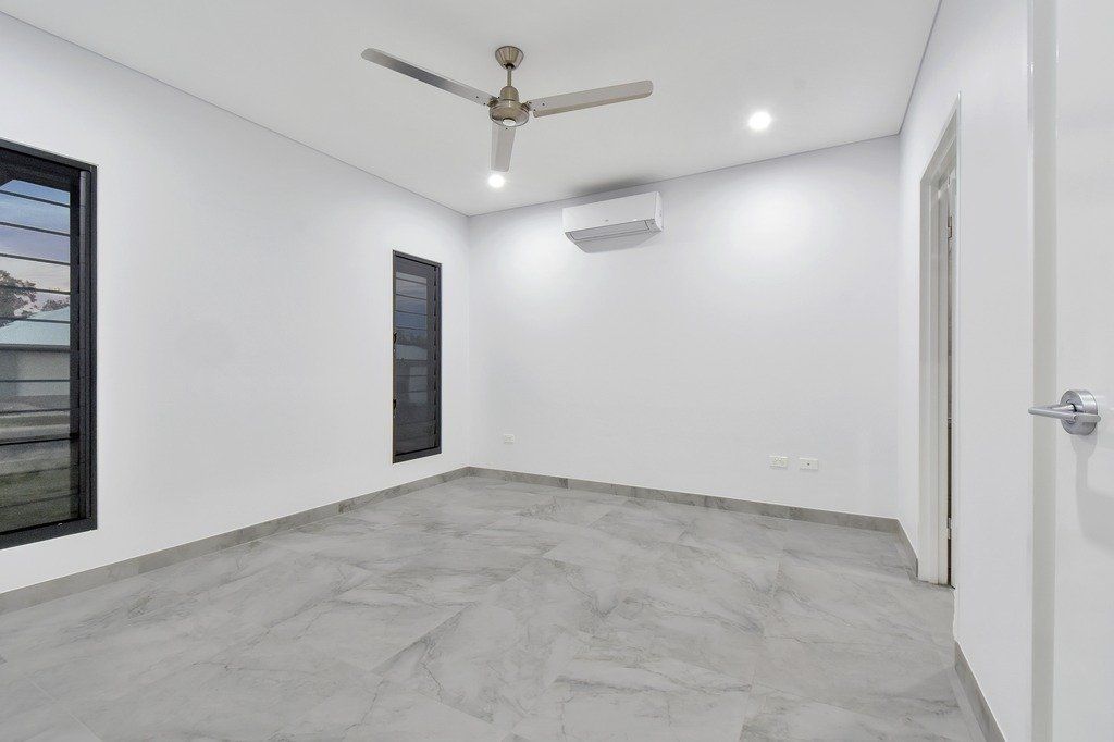 An empty room with a ceiling fan and two windows.