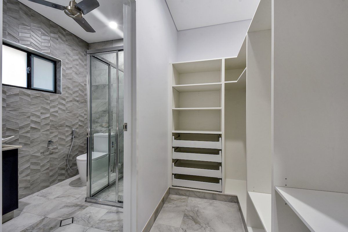 A walk in closet in a bathroom with a toilet and a ceiling fan.