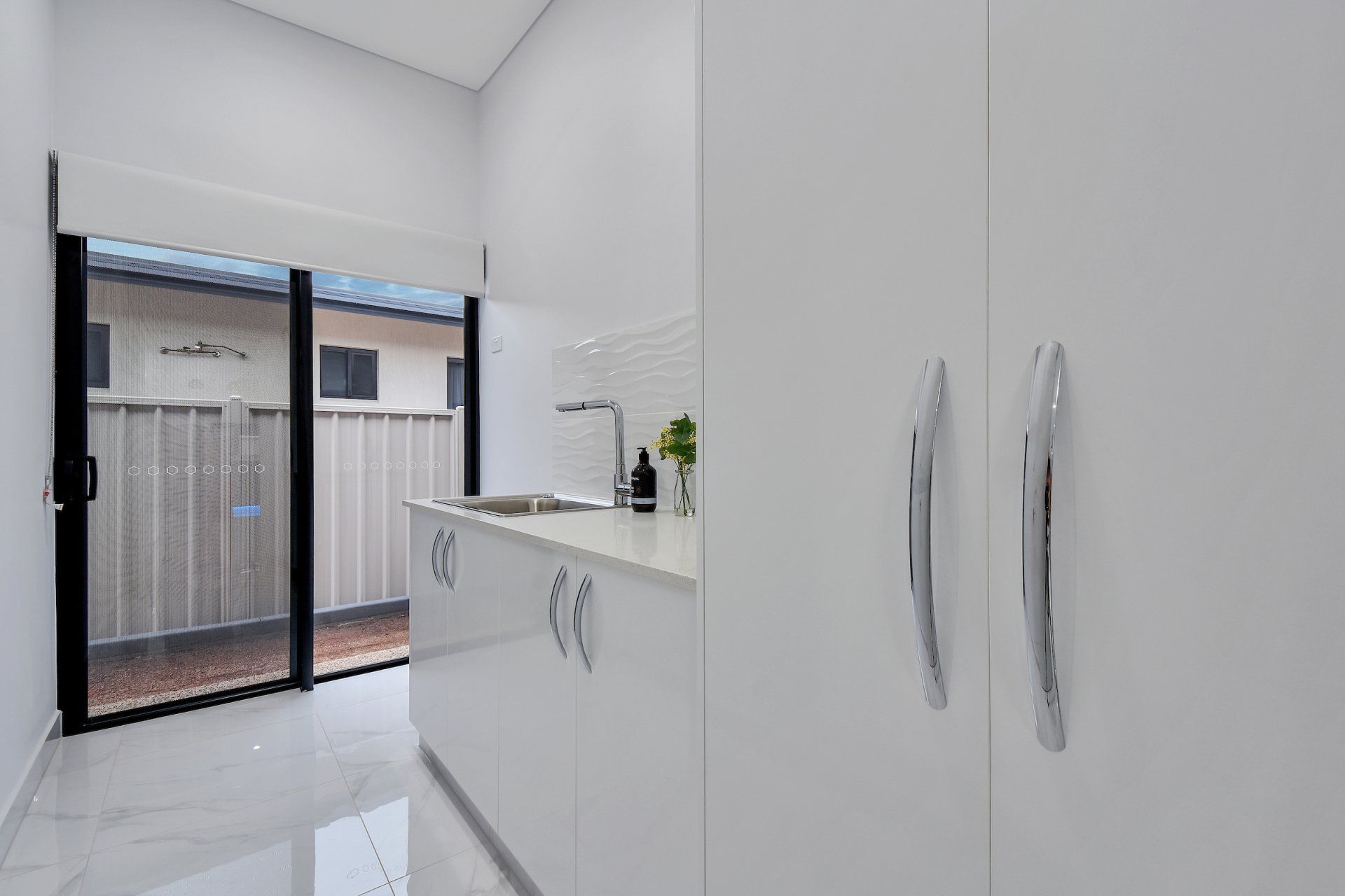 A kitchen with white cabinets , a sink , and a sliding glass door.