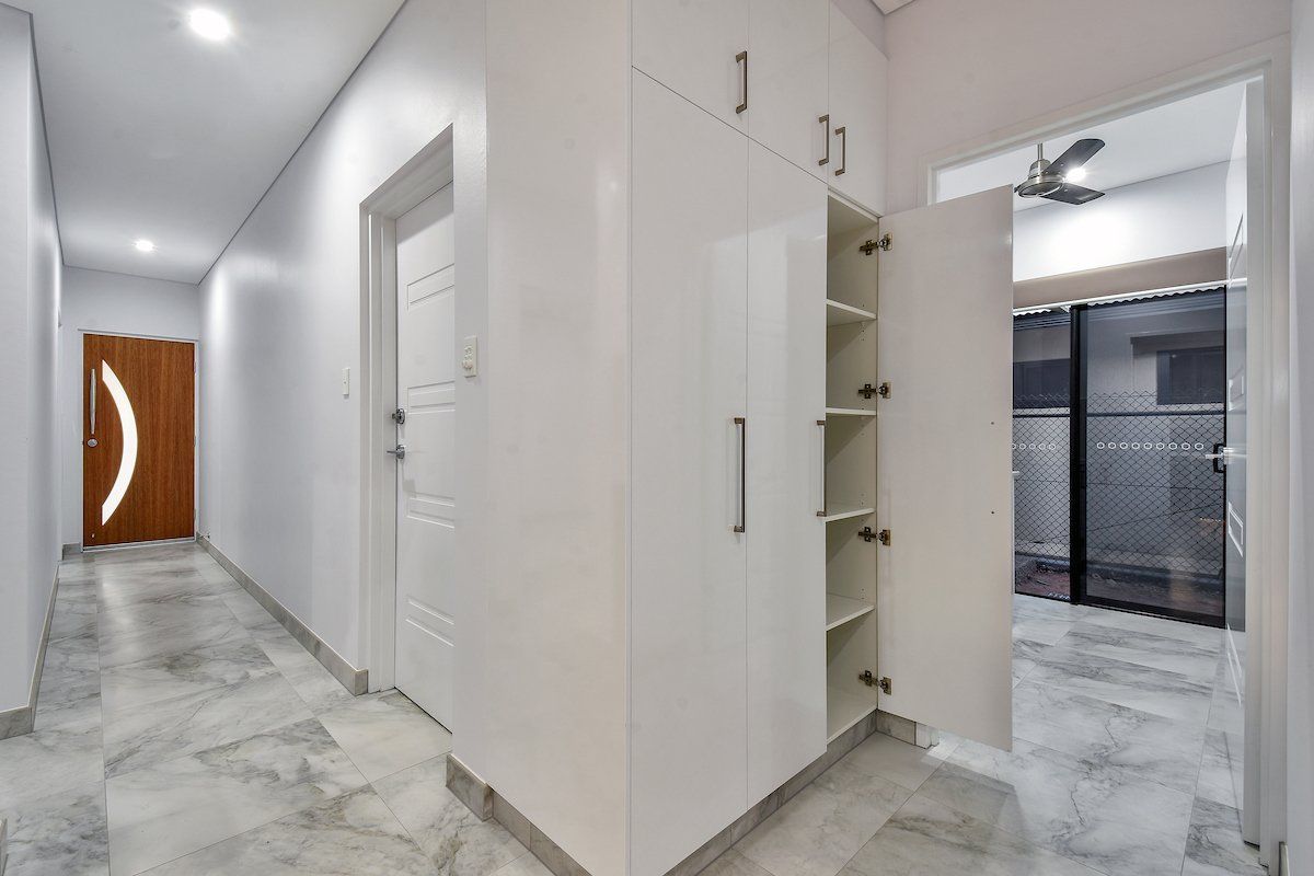 A hallway with white cabinets and shelves and a ceiling fan.