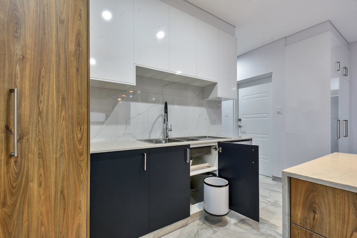 A kitchen with black and white cabinets , a sink , and a trash can.