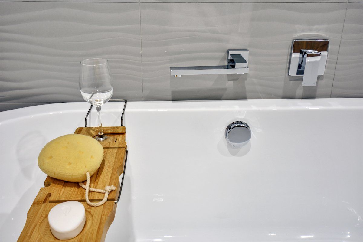 A bathtub with a wooden tray and a glass of wine on it.