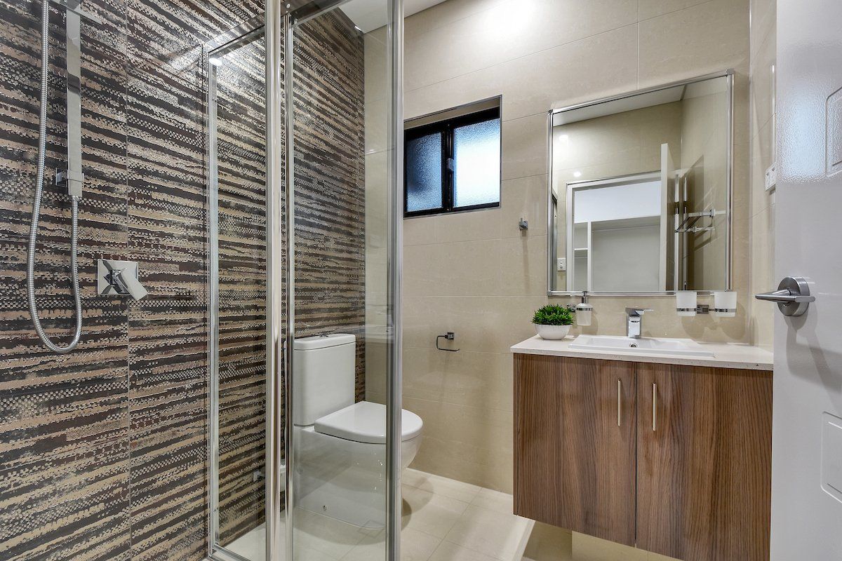A bathroom with a toilet , sink , shower and mirror.