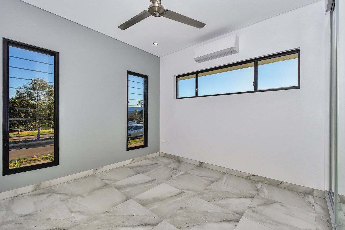 An empty room with a ceiling fan and two windows.