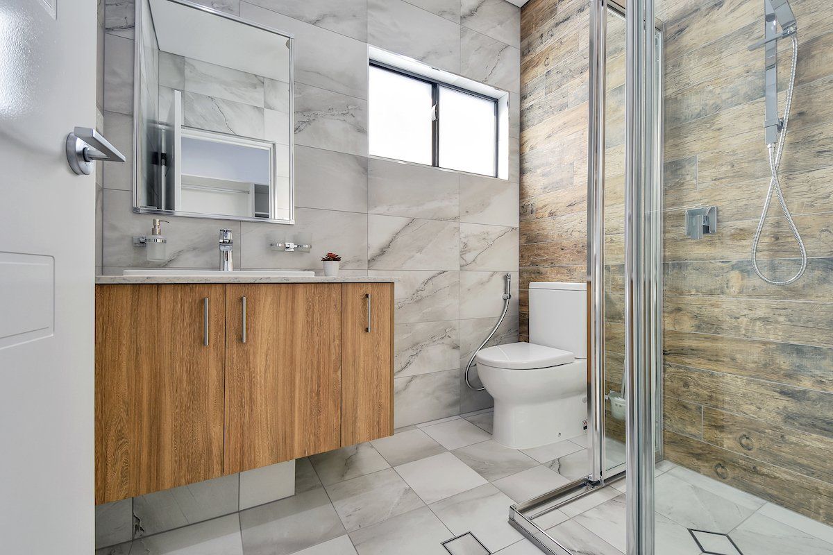 A bathroom with a toilet , sink , mirror and walk in shower.