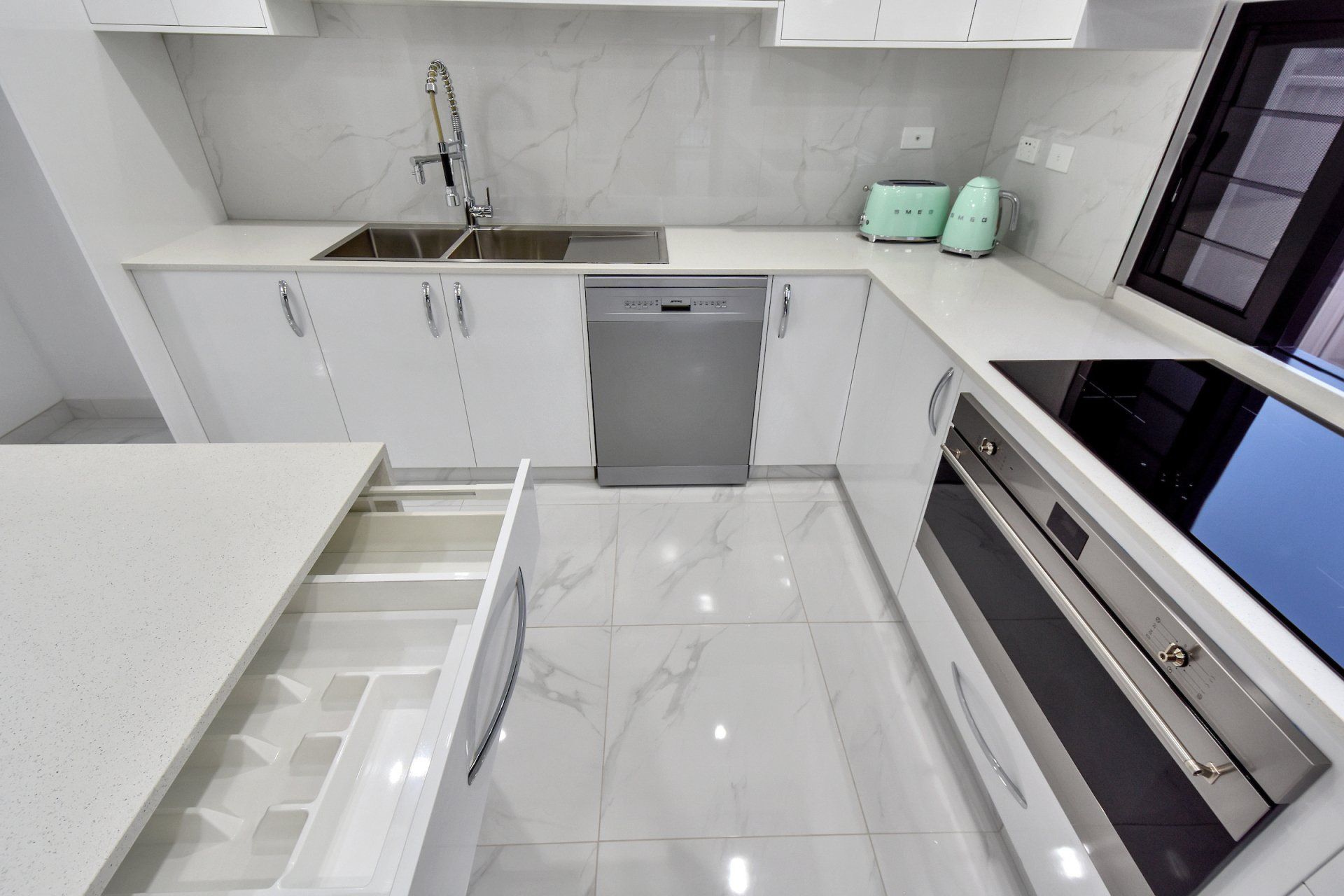 A kitchen with white cabinets , stainless steel appliances , a sink and a dishwasher.