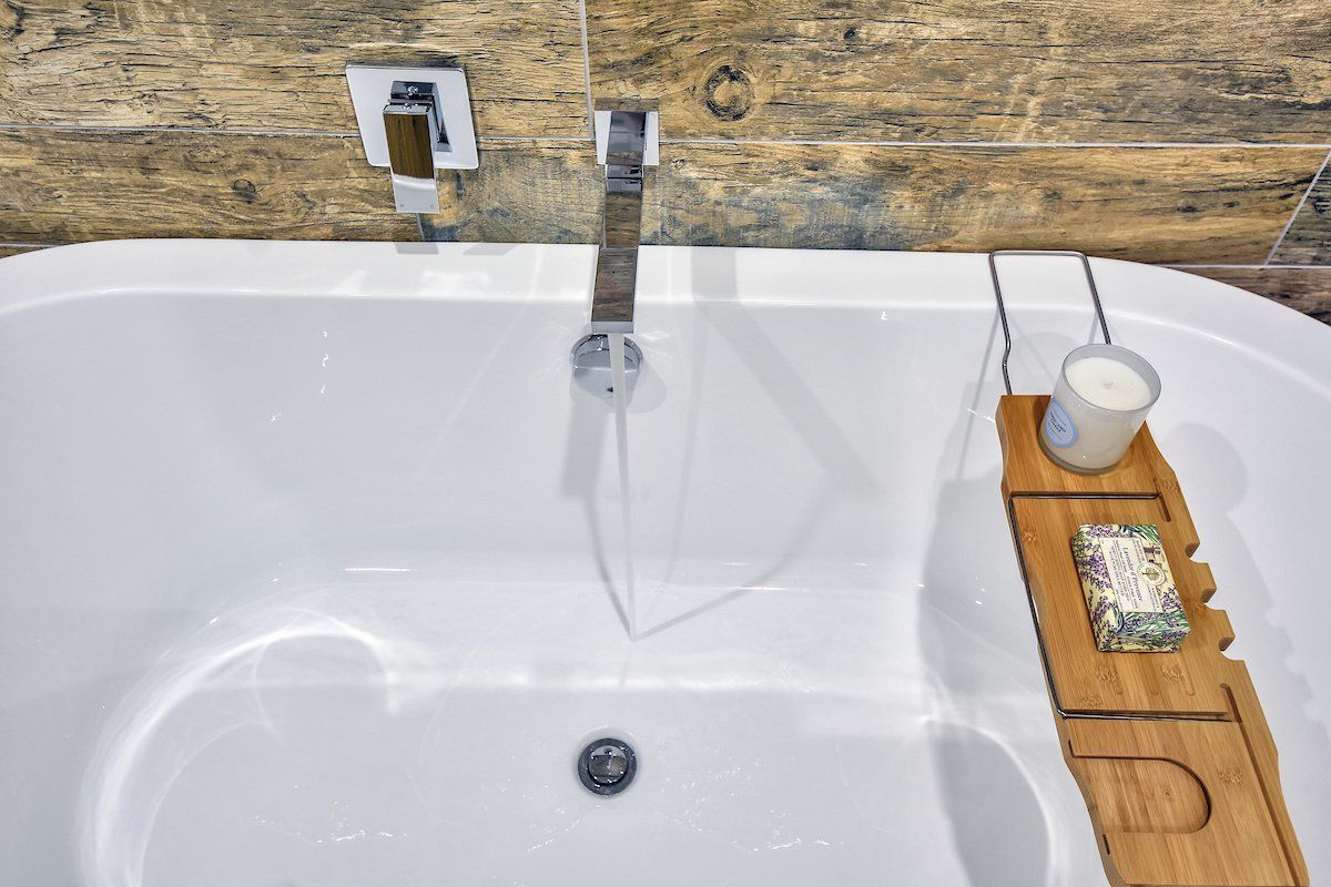 A bathtub with a wooden bathtub tray and a candle on it.