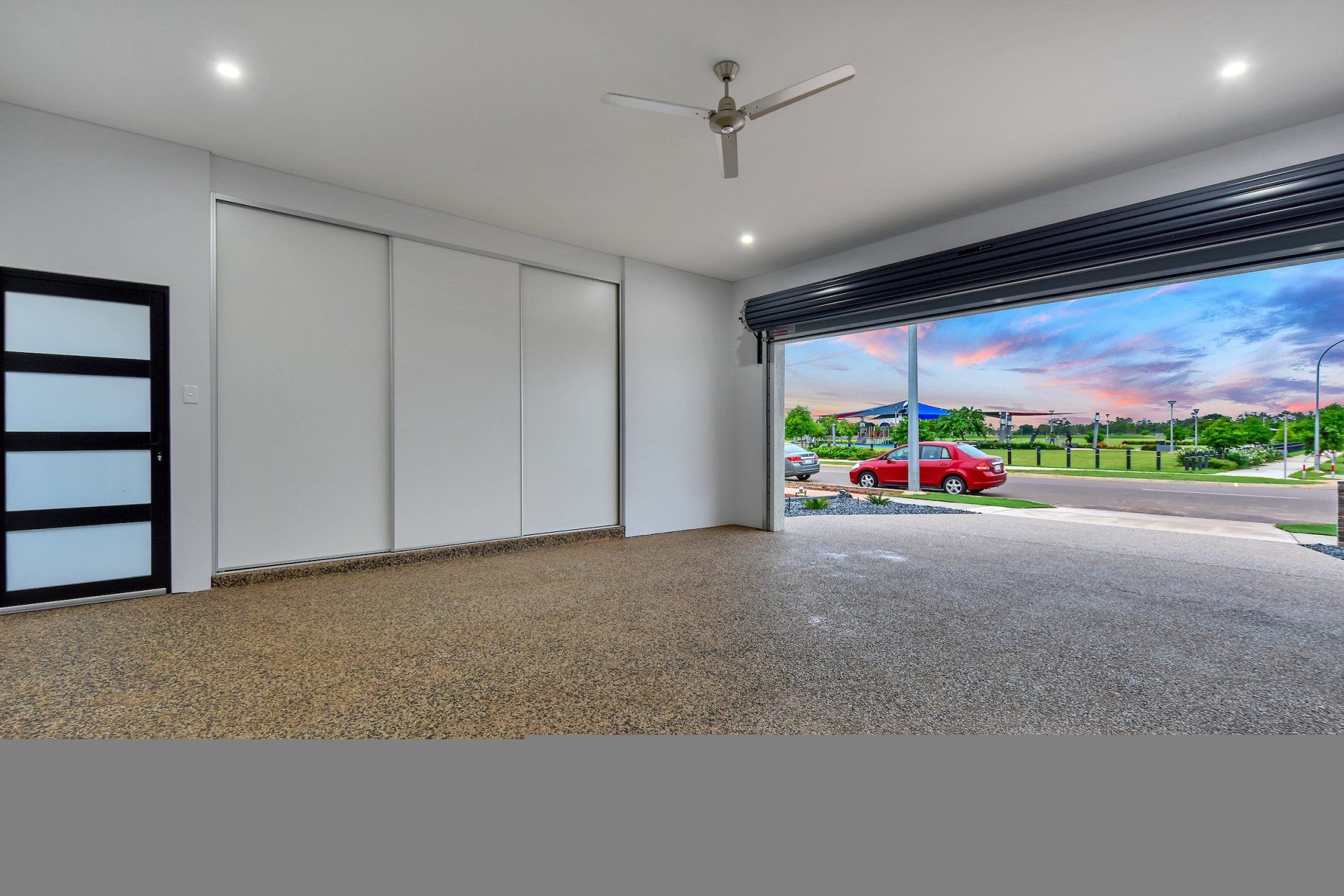 An empty garage with a red car parked in it and a ceiling fan.