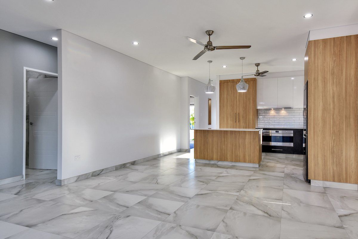 An empty room with a ceiling fan and a kitchen in the background.