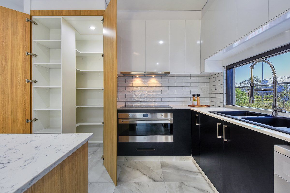 A kitchen with black cabinets , a stove , a sink , and a pantry.