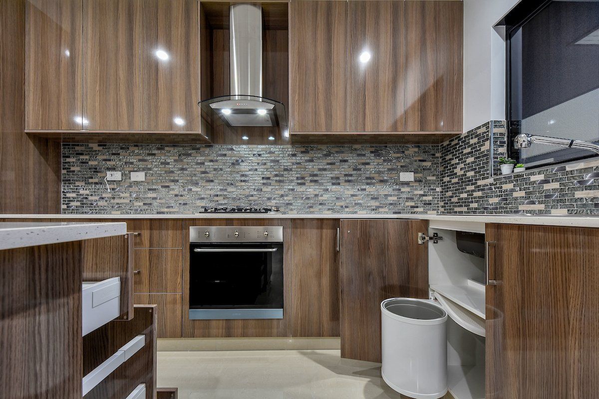 A kitchen with wooden cabinets , a stove , and a trash can.