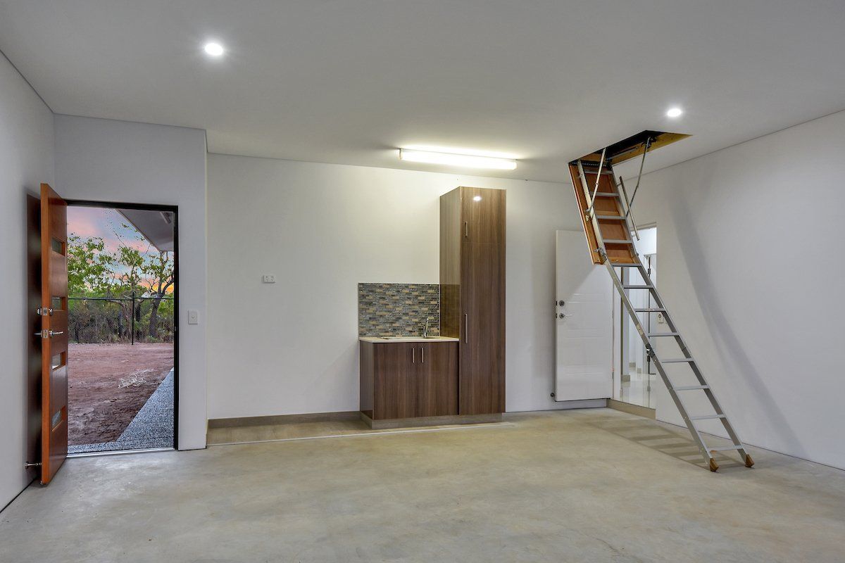 An empty garage with a ladder leading up to the attic.