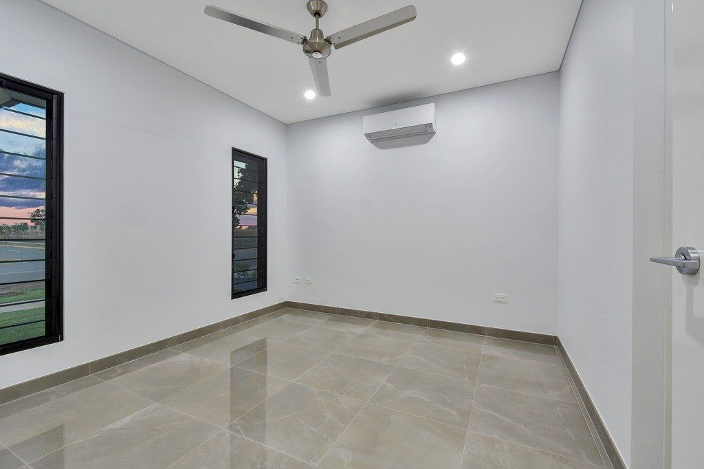 An empty room with a ceiling fan and two windows.