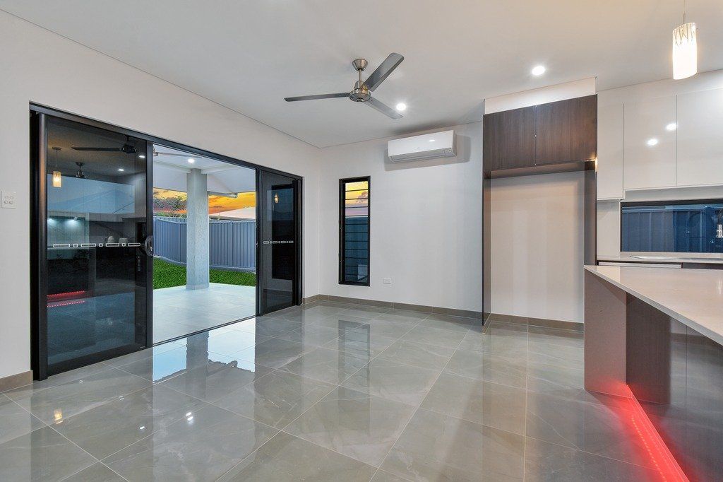 An empty living room with a ceiling fan and sliding glass doors leading to a kitchen.